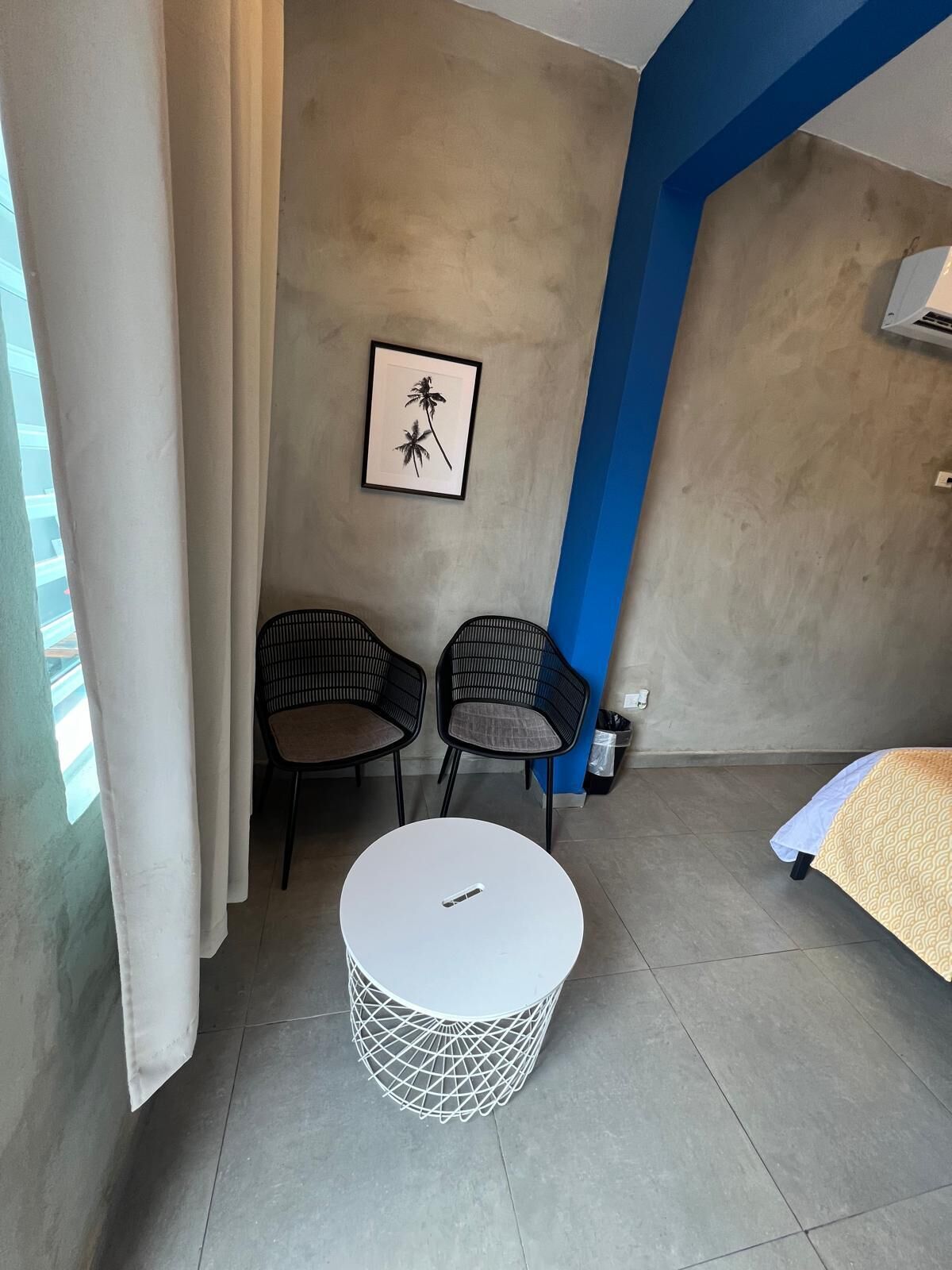 A room with a bed, two chairs, a small round table, and a framed picture on the wall.