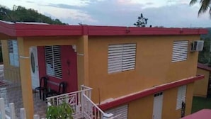 A two-story building with a red roof and yellow walls, featuring a staircase and a small outdoor seating area. - Private Country house 5 miles from beach (Aguada)