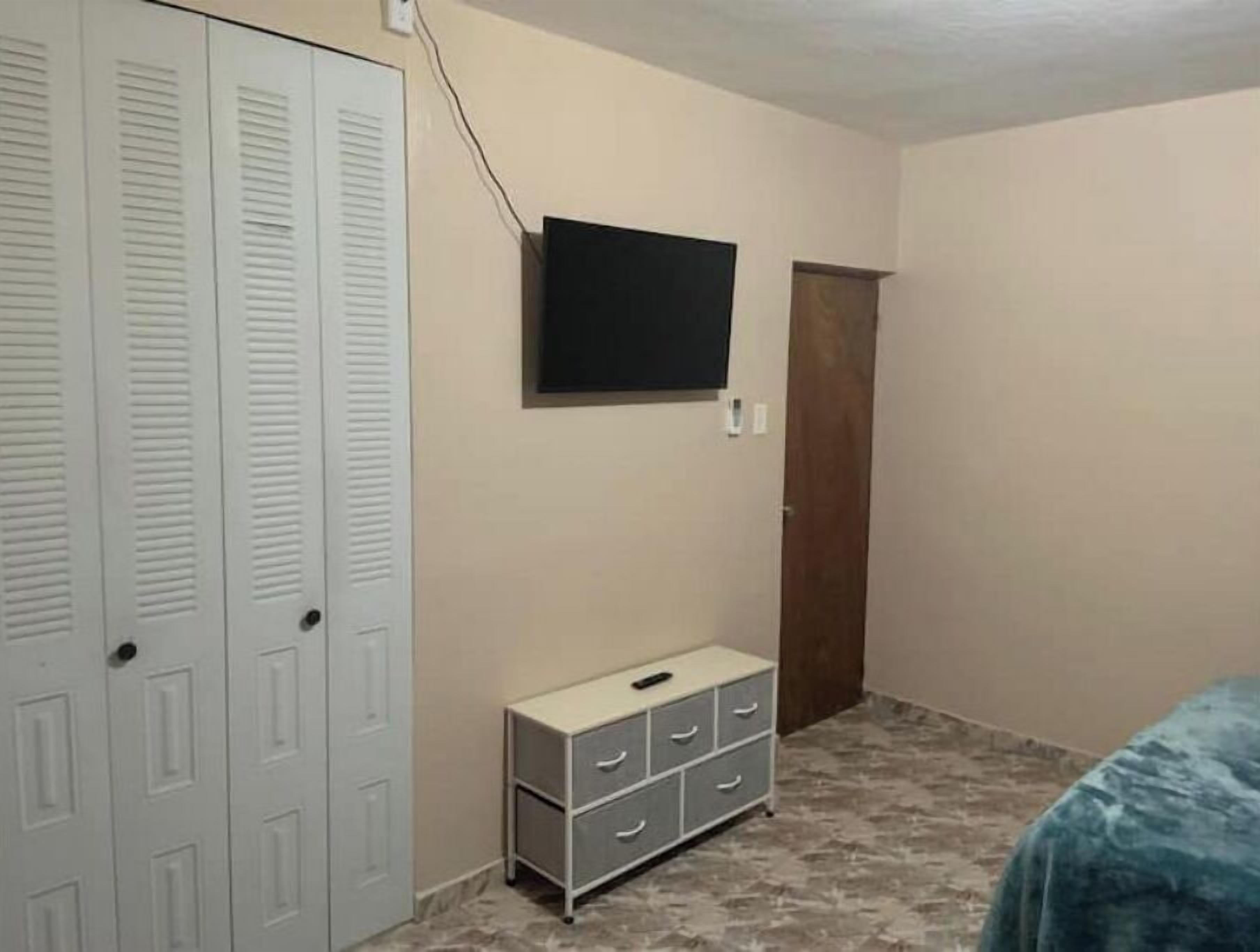 Une chambre avec un placard, un téléviseur fixé au mur et une petite commode.