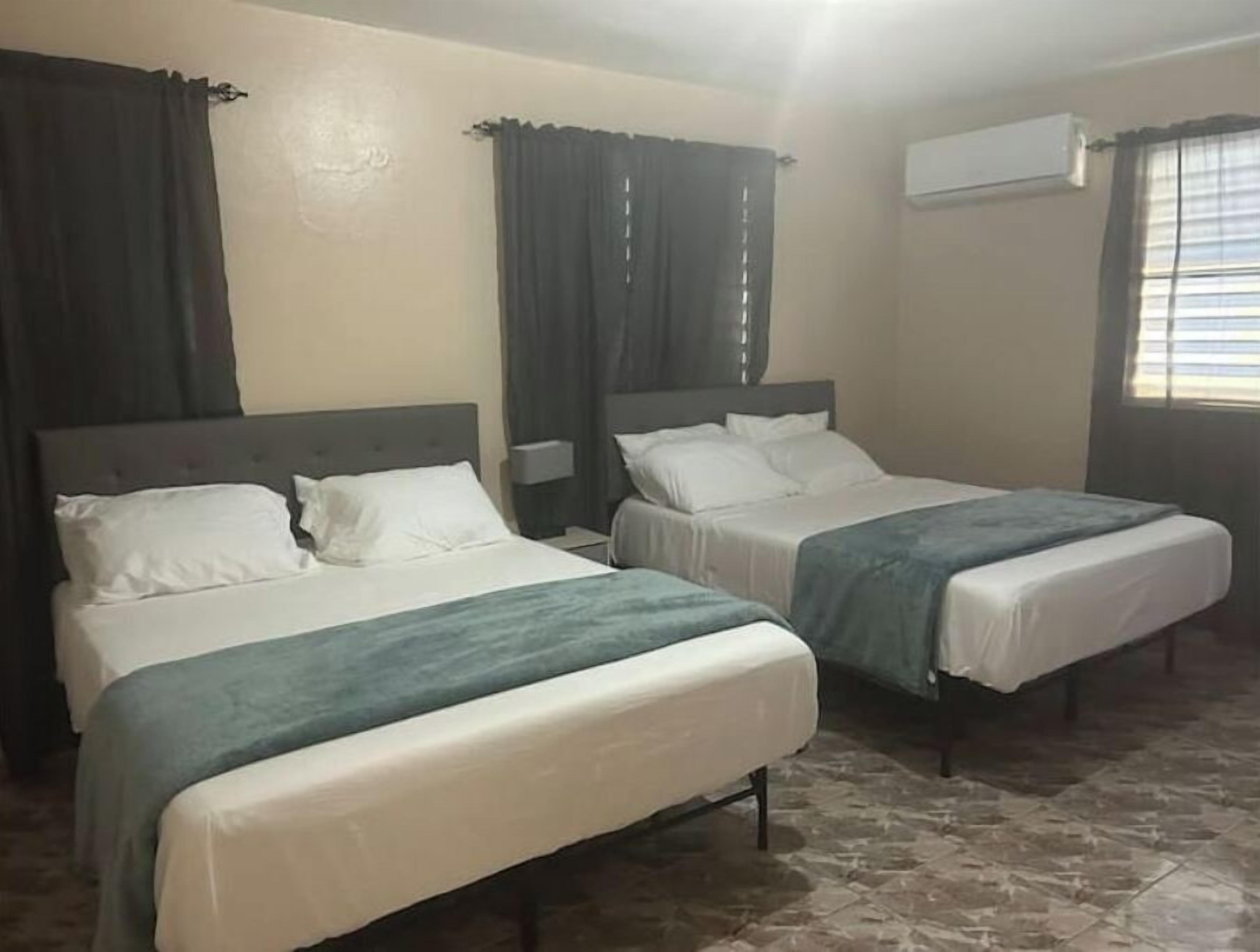 Ein Hotelzimmer mit zwei Einzelbetten, einem Nachttisch, einer Klimaanlage und einem Fenster mit Jalousien.