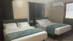A hotel room with two single beds, a nightstand, an air conditioning unit, and a window with blinds. - Private Country house 5 miles from beach (Aguada)