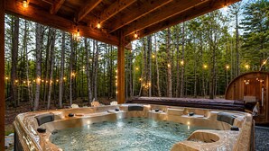 Un jacuzzi con cubierta de madera y luces de cadena, rodeado por un bosque.