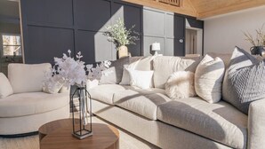 Una sala de estar moderna con un sofá color beige, una mesa redonda de madera y un florero con flores blancas.