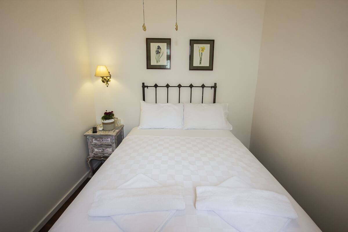 A neatly made bed with a checkered bedspread, a bedside lamp, and two framed pictures on the wall.