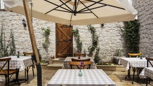 An outdoor patio with checkered tablecloths, wooden chairs, and a large umbrella. - OPUS 1910 OTEL (Ayvalik)