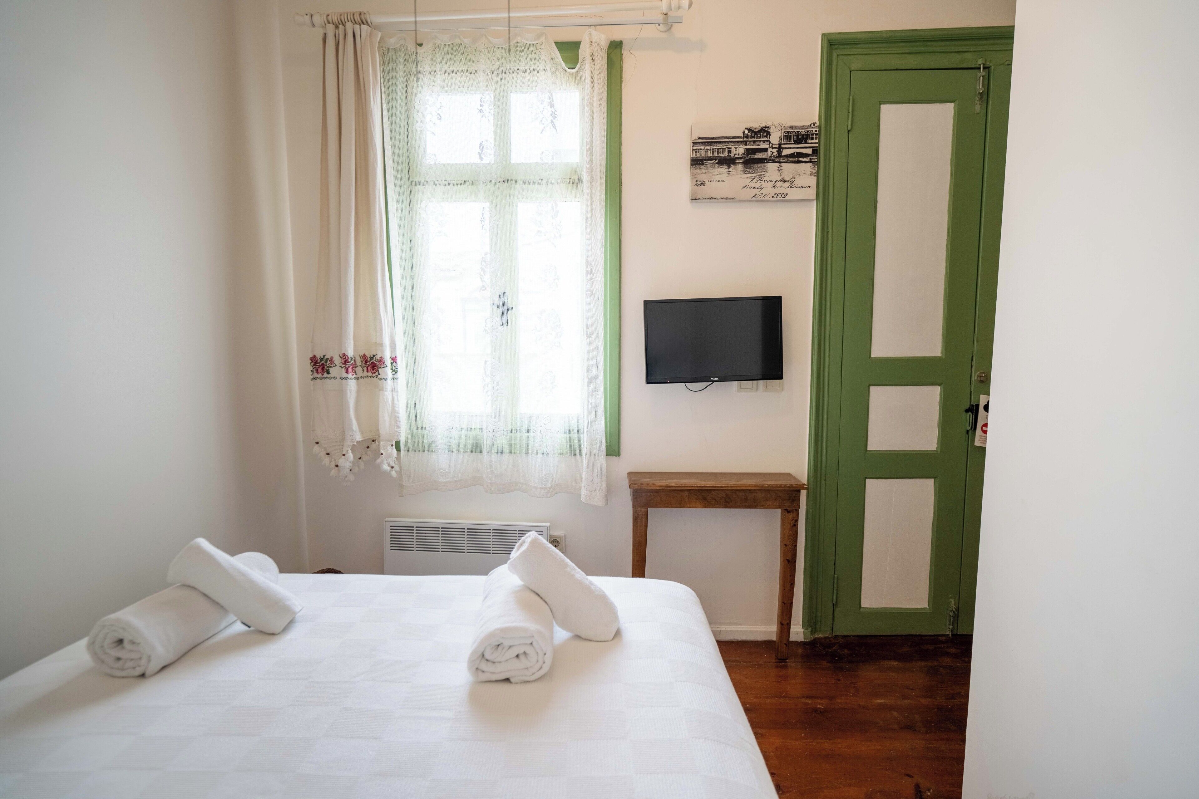Una camera da letto con un letto, una televisione, una porta verde e una finestra con tende.