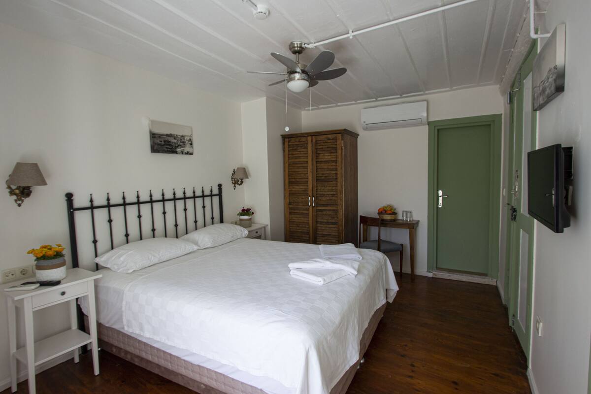 A bedroom with a bed, a nightstand, a wooden wardrobe, a green door, and a ceiling fan.