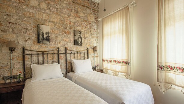 A room with two beds, a stone wall, and a window with curtains. - OPUS 1910 OTEL (Ayvalik)