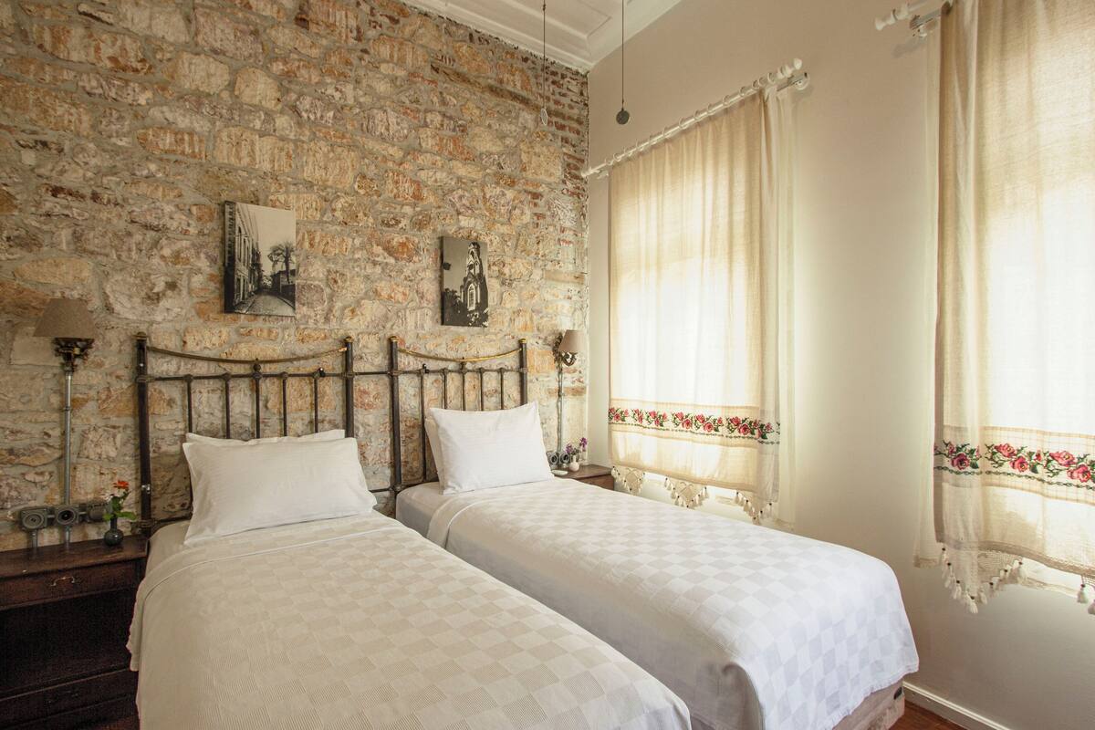 A room with two beds, a stone wall, and a window with curtains.
