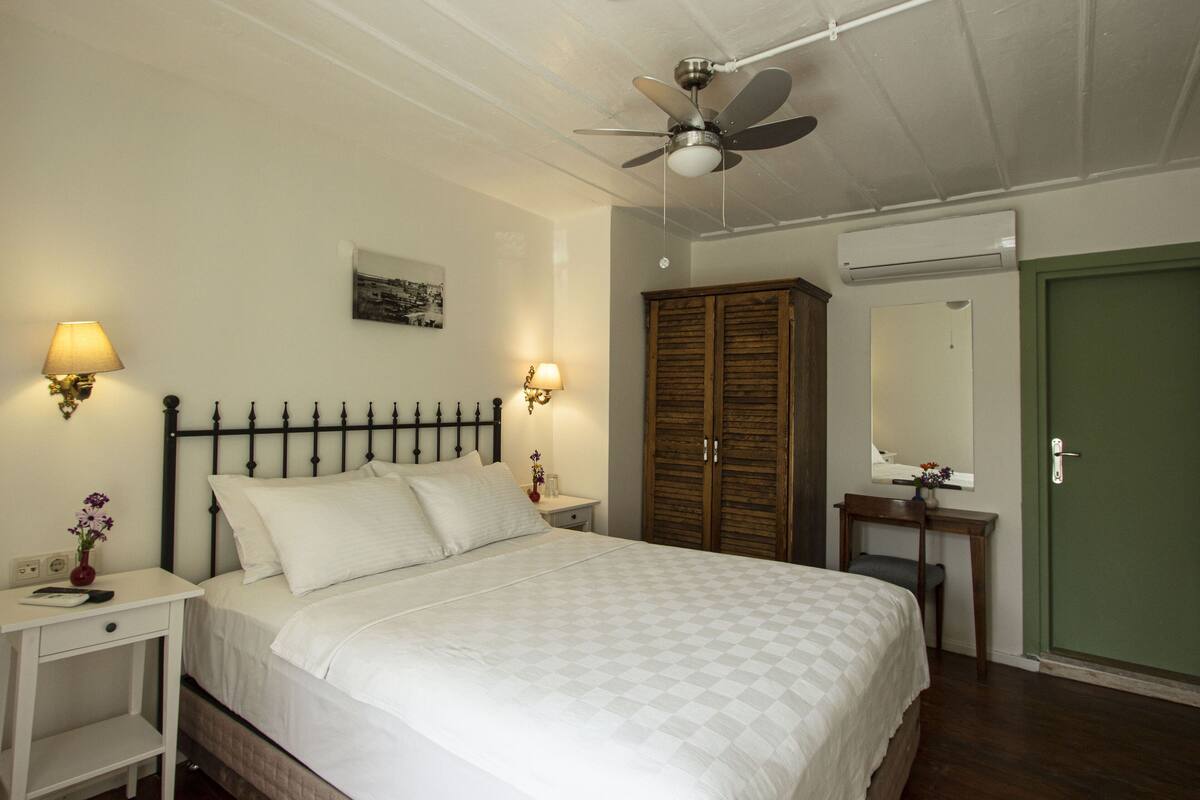 A bedroom with a bed, bedside lamps, a wardrobe, a mirror, and a ceiling fan.