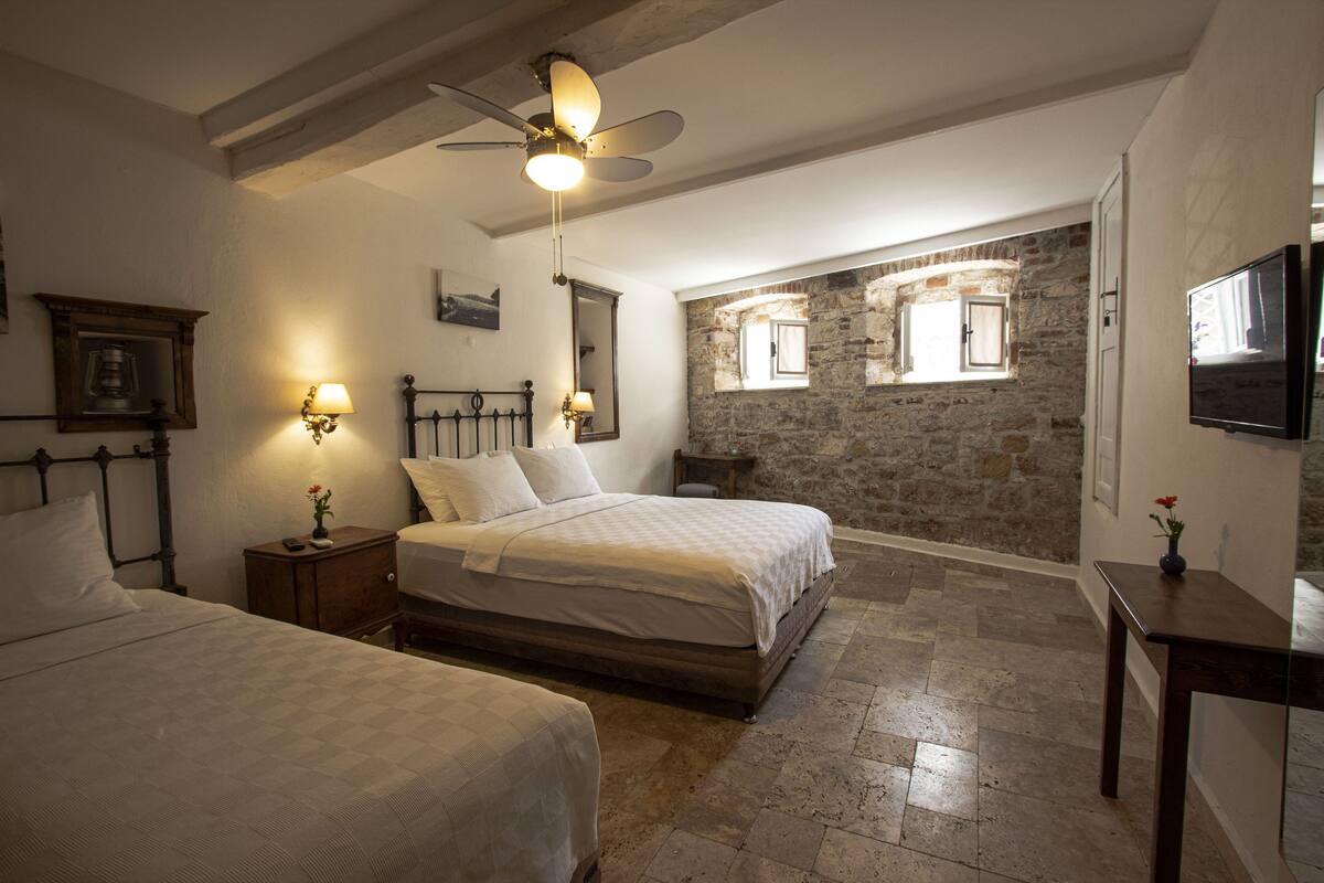 A bedroom with two beds, a ceiling fan, stone walls, and a television.