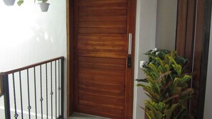 A wooden door with a metal handle, a small potted plant to the left, and a larger plant to the right. - De Padma Villa Gili Air (Gili Air)