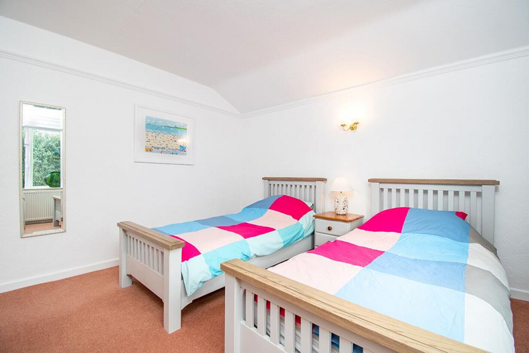 Un dormitorio con dos camas individuales, una mesita de noche, una lámpara, una ventana y un cuadro en la pared.