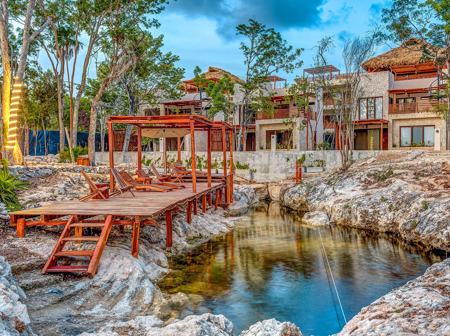 A resort with a wooden deck, a small water feature, and modern buildings with thatched roofs.