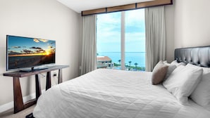 Camera da letto con un letto grande, una TV su un mobile in legno e vista mare attraverso ampie finestre.