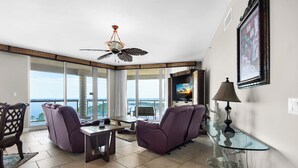Un ampio soggiorno con una grande finestra vista oceano, una ventola a soffitto e un televisore su un mobile.