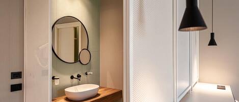 A modern bathroom with a wooden vanity, a round mirror, and a black pendant light.