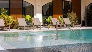 Une piscine dotée de chaises longues et un bâtiment moderne avec de grandes fenêtres et des lambris en bois verticaux.