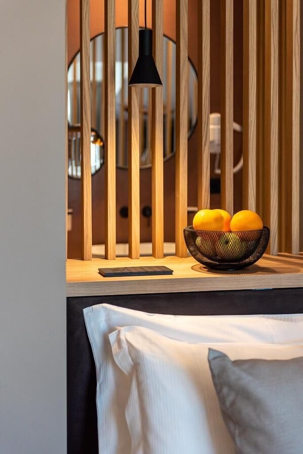 A bed with a white sheet and pillows, a wooden slat headboard, a black pendant light, and a basket of oranges on the bedside table. - Limen Wellness Hotel (Campofelice di Roccella)