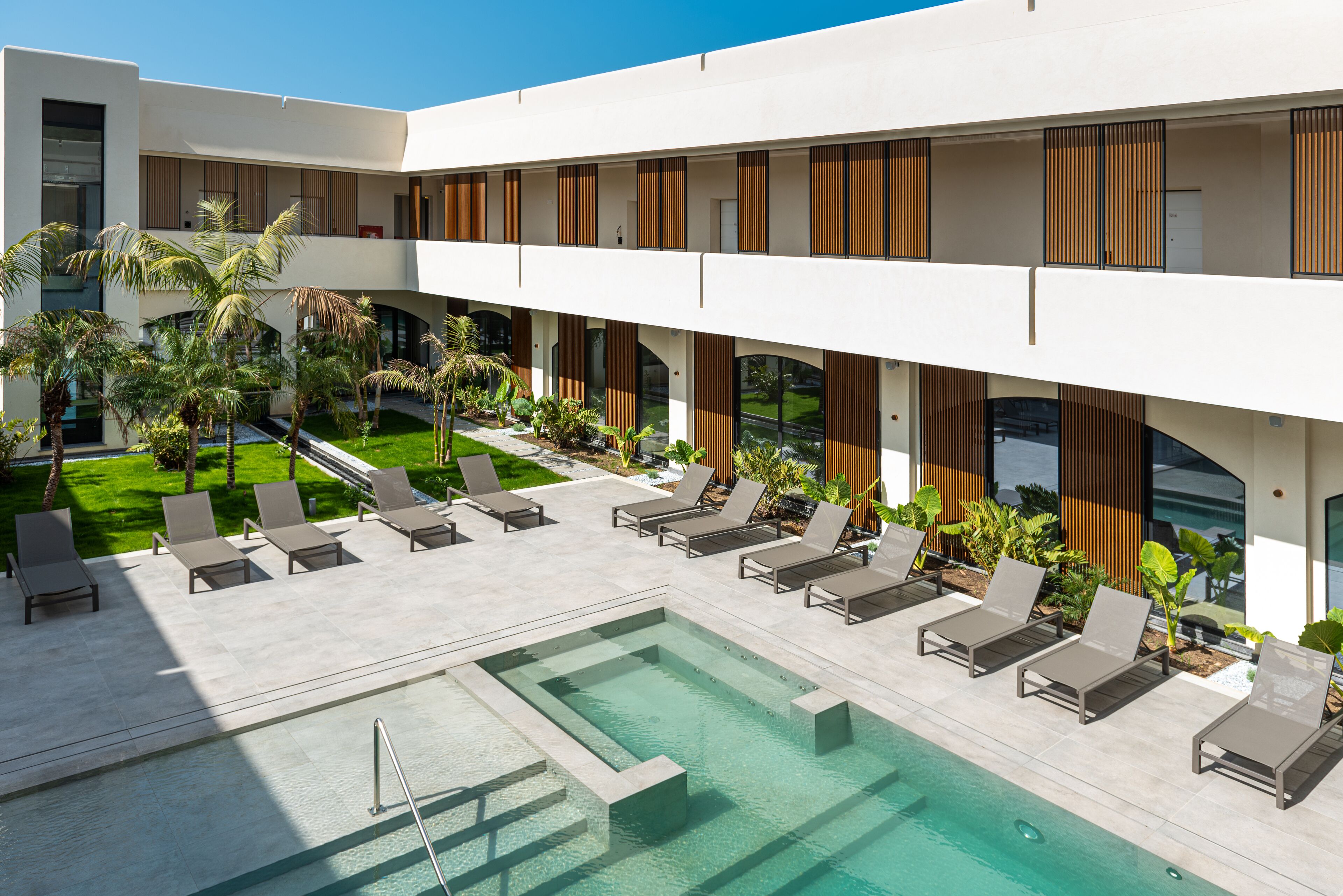 A modern hotel with a pool area, lounge chairs, and a well-maintained garden.