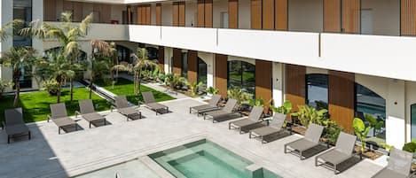 A modern hotel with a pool area, lounge chairs, and a well-maintained garden.