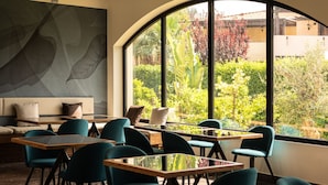 Un intérieur moderne avec une grande fenêtre en arc de cercle, un canapé avec des coussins, ainsi que plusieurs tables et chaises disposées pour les repas ou le travail.