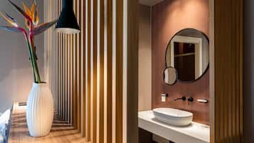 A modern bathroom with a white sink, a round mirror, and a tall vase with a plant.