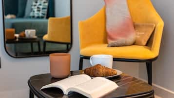 Um recanto aconchegante para leitura, com uma mesa pequena, um livro, um croissant e uma xícara.