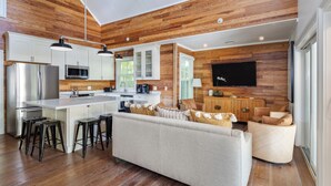 A modern kitchen with wooden paneling, a central island with stools, a built-in microwave, and a large flat-screen TV mounted on the wall.