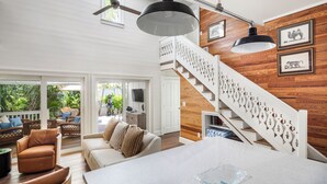 A spacious living area with a high ceiling, a wooden staircase, and a balcony with outdoor furniture.
