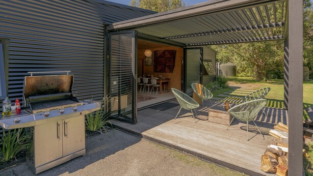 Un patio moderno al aire libre con una parrilla, zona de estar y un espacio cubierto que conduce a un comedor.