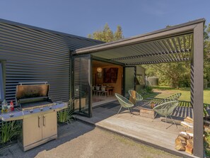Eine moderne Außenpatio mit Grill, Sitzgelegenheit und überdachtem Bereich, der zu einem Essbereich führt.