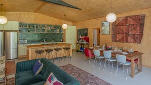 Amplia sala de estar con un sofá verde, una mesa de comedor de madera dispuesta para seis personas y una cocina con salpicadero verde.