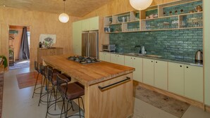 Una cocina moderna con una isla de madera, taburetes de bar, un refrigerador de acero inoxidable y un salpicadero de azulejos verdes.
