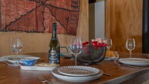 Una mesa de comedor dispuesta con platos, vasos, una botella de vino y una cesta de flores.