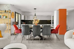 Un soggiorno moderno con zona pranzo, cucina sullo sfondo e una grande parete d'accento arancione.