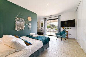 Une chambre à coucher moderne avec un lit, un attrape-rêves fixé au mur, une télévision et une vue sur l’extérieur.