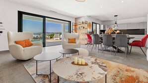 Una sala de estar moderna con un ventanal grande, un comedor con una silla roja y una cocina al fondo.