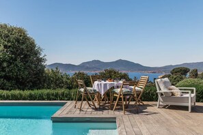 Area piscina con tavolo e sedie, una poltrona prendisole e vista sul mare e sulle montagne.