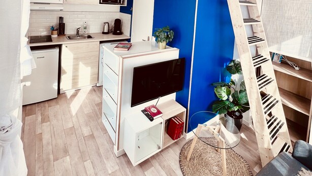 A compact, modern apartment with a kitchenette, a dining area, and a loft bedroom with a blue accent wall. - De la Terre à la Lune (Amiens)