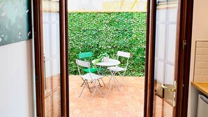 An open door leading to a patio with a table and chairs, a green hedge, and a blue mat on the floor. - L'Ile Mystérieuse - Studio avec Terrasse (Amiens)