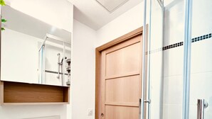 A bathroom with a wooden door, a glass shower enclosure, and a white sink with a mirror above it. - L'Ile Mystérieuse - Studio avec Terrasse (Amiens)