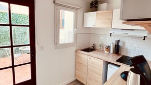 A modern kitchen with light wood cabinets, a black countertop, and a stainless steel kettle. - Tour du monde en 80 jours - Studio avec Terrasse (Amiens)