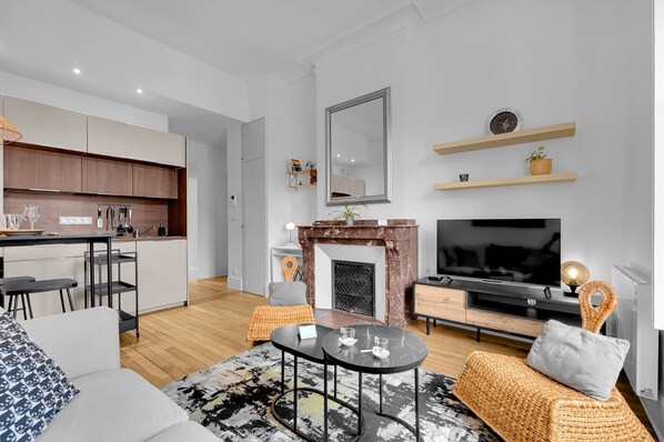 A modern living room with a fireplace, a TV, and a kitchen area.