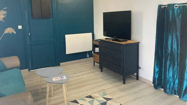 Una sala de estar con una pared azul, un televisor de pantalla plana sobre un mueble de madera, una mesita redonda y una alfombra estampada.