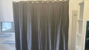 Una habitación con una cortina gris, un televisor de pantalla plana montado en la pared y un estante blanco.