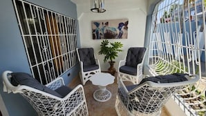Un balcone con mobili in vimini bianco, tra cui due sedie e un tavolino, e una pianta in vaso.