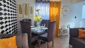 Un'area da pranzo con tavolo in vetro, sedie imbottite scure e un vaso con fiori gialli.
