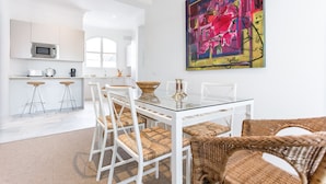 A modern kitchen with white cabinets, a microwave, and a coffee machine. There is a dining area with a glass table and wicker chairs. - Adriano 2.1 by Home at Homes (Sevilla)