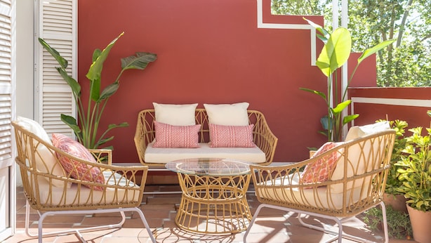 A patio with wicker furniture, a glass table, and a red wall. - Adriano 2.1 by Home at Homes (Sevilla)